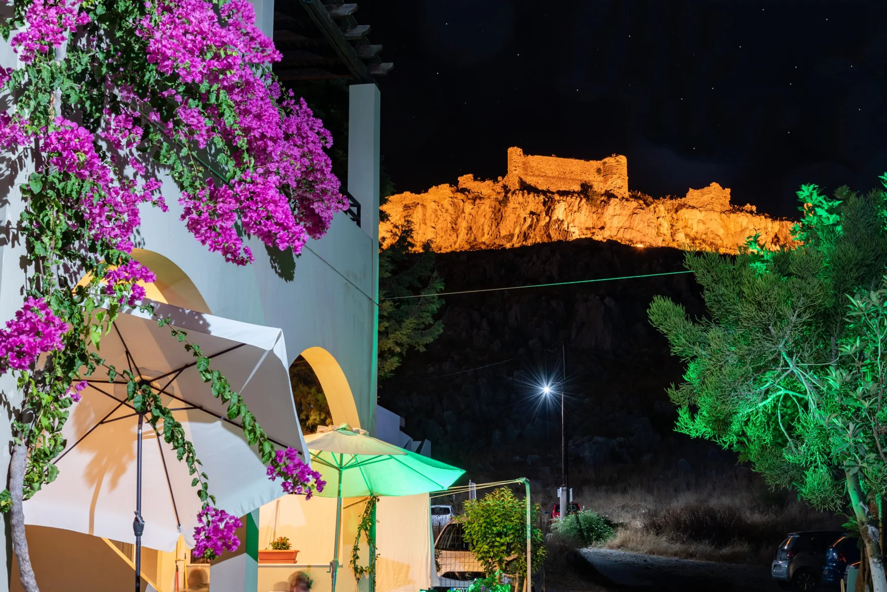 Bougainvillea at Haraki Sand Beach with illuminated Feraklos Castle